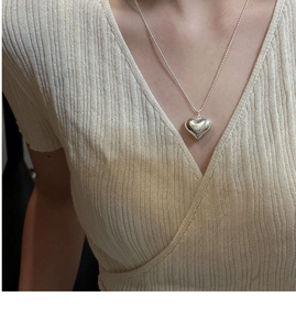 Detail of a polished silver heart pendant necklace worn on a beige ribbed V-neck top