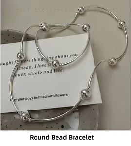 Detail view of a layered S925 sterling silver beaded bracelet on a minimalist ceramic plate