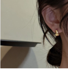 Close-up of a minimalist golden water drop stud earring on a female model ear