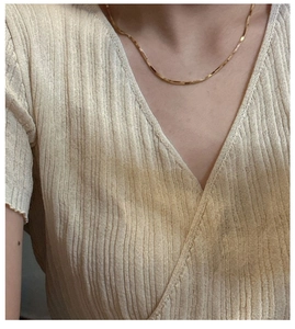 Close-up of minimalist gold snake chain necklace worn with a beige ribbed knit sweater