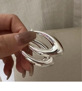 Gros plan de boucles d'oreilles créoles larmes en argent portées sur un tissu beige