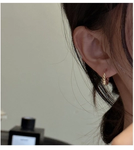 Close-up of stylish gold croissant hoop earrings with a twisted metallic texture on ear