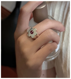 Detail of S925 sterling silver flower ring with a red gemstone on a model's finger