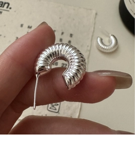 Macro shot of silver croissant hoop earrings with textured twisted metal design