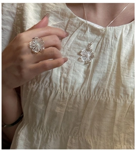 Détail de la bague et du collier en argent aux motifs floraux portés sur fond de tissu beige