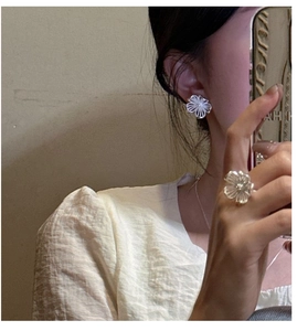 Detail von silbernen Hohlblumenohrringen und offenem Ring Set getragen von einer Frau