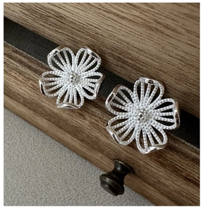 Gros plan de boucles d'oreilles fleurs en argent S925 avec texture perlée sur bois