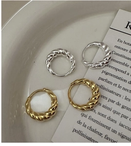 Detail of twisted hoop earrings in gold and silver finish on a ceramic tray