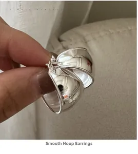 Macro detail of glossy S925 silver oval hoop earrings held against a soft fabric background