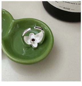 Detail of adjustable silver flower ring featuring a round purple gemstone in a ceramic dish