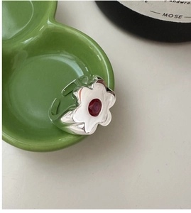 Detail of flower shaped silver ring with red gemstone on a green ceramic dish