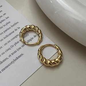 Elegant gold twisted rope hoop earrings on a white ceramic plate with French text