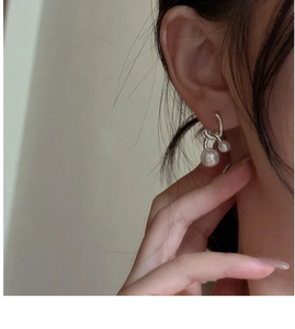 Close-up of S925 silver cross earrings with two elegant white pearls worn on ear