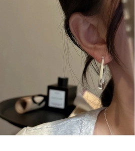 Close-up of minimalist silver oval drop earrings worn by a model in a retro setting