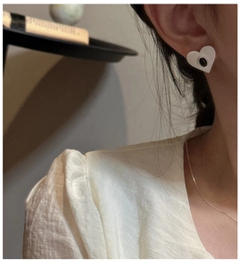 Close-up of heart-shaped matte earrings featuring a black oval center on a model