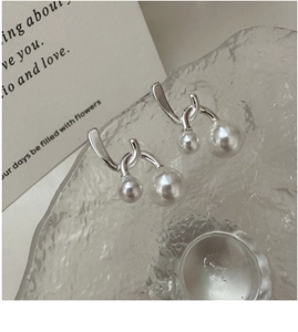 Detailed view of silver crossover pearl earrings on textured glass with soft lighting
