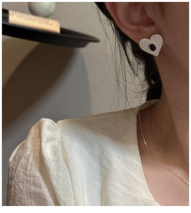 Detail of a minimalist heart-shaped stud earring with a black oval stone inlay on a model