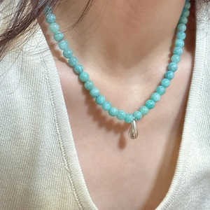 Close-up of mint blue beaded necklace with silver waterdrop pendant worn by a model