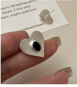 Macro shot of silver heart earrings with brushed finish and black gemstone inlay detail