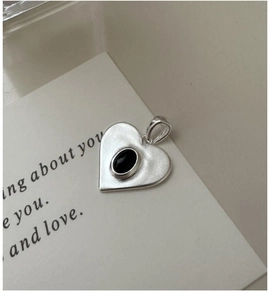 Détail d'un pendentif cœur en argent mat avec insert noir sur fond de carte minimaliste