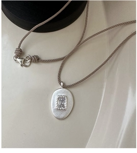 Détail d'un pendentif ovale en argent mat avec zircon sur un cordon tressé marron