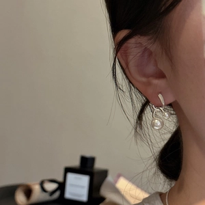 Minimalist S925 silver cross pearl earrings worn on ear in a cozy, elegant setting