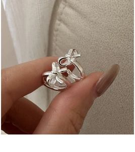 Macro detail of silver S925 bow-shaped hoop earrings worn on hand with linen background