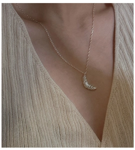 Close-up of a silver croissant pendant necklace on a beige knit sweater texture
