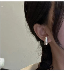 Close-up of minimalist S925 sterling silver water drop earrings worn on ear