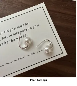 Detail of S925 sterling silver pearl earrings on a poetic card and dark wood background