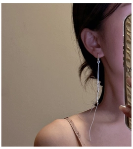 Detail of silver long tassel earrings with beads worn by a model in a close-up shot