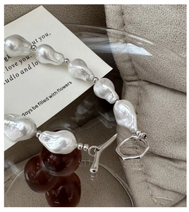 Close-up of Baroque pearl necklace with silver T-bar clasp on a beige fabric background