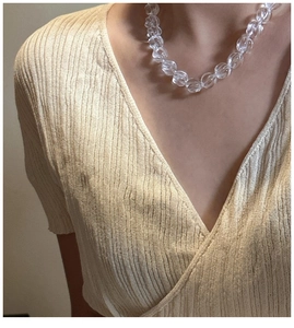 Close-up of twisted clear crystal bead necklace on model with beige V-neck shirt