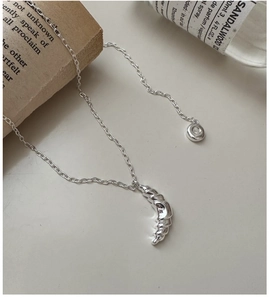 Macro view of a S925 silver croissant pendant necklace styled with vintage props