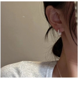 Macro shot of minimalist silver U-shaped earring with elegant white round pearl on ear