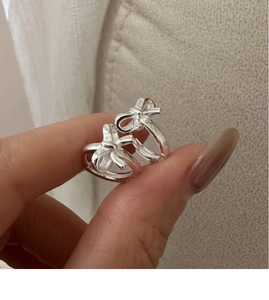 Detailed close-up of a silver bow earring held by hand against a soft fabric background