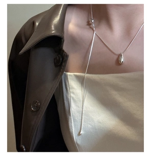 Detailed close-up of a silver water drop pendant necklace worn on a leather jacket outfit