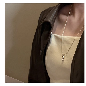 Close-up of golden teardrop pendant on fine chain necklace worn with autumn style outfit