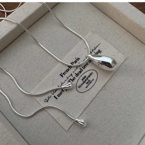 Detailed view of S925 silver teardrop pendant and snake chain on beige fabric
