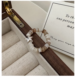 Detail of S925 silver star charm on tri-color beaded elastic ring over jewelry box