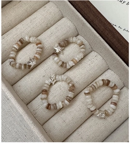 Close-up of four elastic bead rings with shell discs and metal star charms on velvet