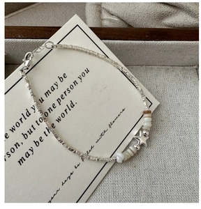 Dettaglio della collana con stella in argento S925 e perline su sfondo in tessuto grigio