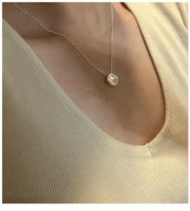 Minimalist irregular pebble pendant silver necklace worn on a collarbone by a female model