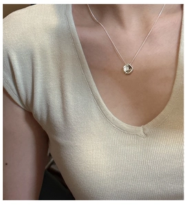 Close-up of a silver irregular textured round pendant necklace on a knit sweater