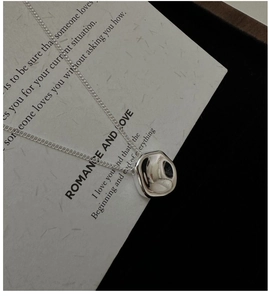 Macro shot of irregular square silver pendant with polished mirror finish on poetic paper