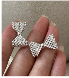 Detailed close-up of S925 silver bow earrings with textured bead surface and metallic finish