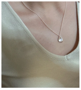 Collier avec pendentif goutte en argent irrégulier porté sur un pull en maille dorée