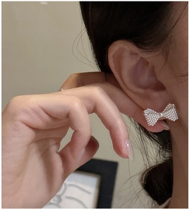 Close-up of S925 sterling silver bow earrings with detailed beaded texture on a model