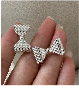 Macro detail of S925 sterling silver bow earrings with textured micro-beaded metal surface