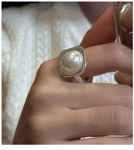 Detail view of a large white Mabe pearl set in a square silver ring worn by a model